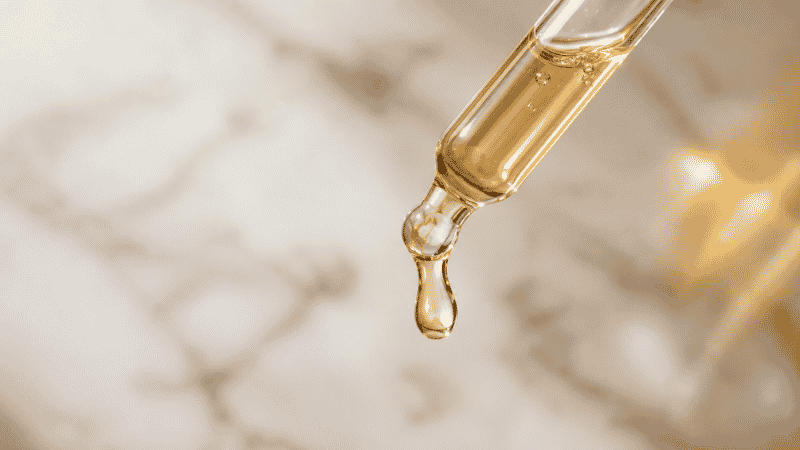 A drop of luxury anti-aging serum on a glass dropper — retinoids and peptides for skin elasticity
