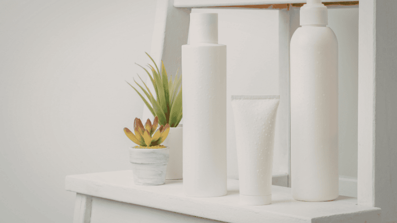 A curated luxury skincare shelf featuring minimalist blue and silver bottles of serums and moisturizers against a backdrop of a high-end white marble bathroom.