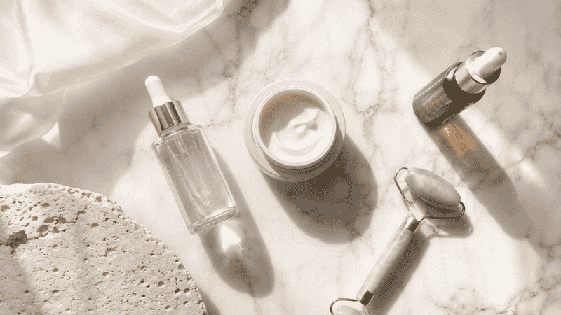 Luxury skincare routine products for aging skin arranged on marble — serum, moisturiser, SPF and facial roller