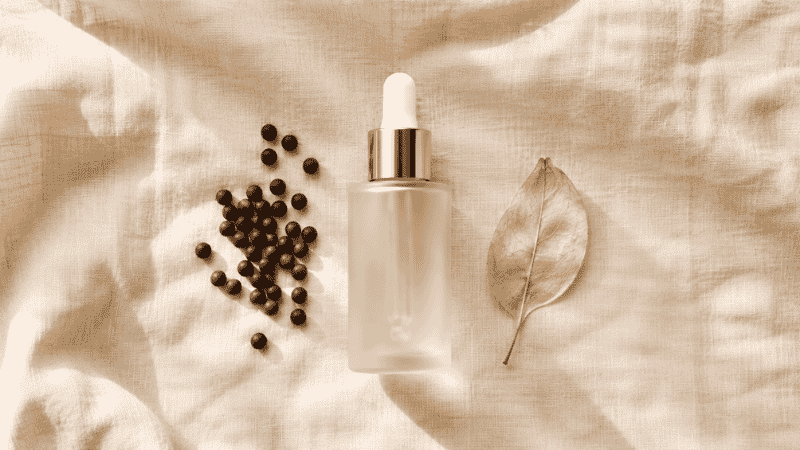 Luxury bakuchiol serum in frosted glass dropper beside psoralea corylifolia seeds on ivory linen — bakuchiol serum guide for mature aging skin as retinol alternative
