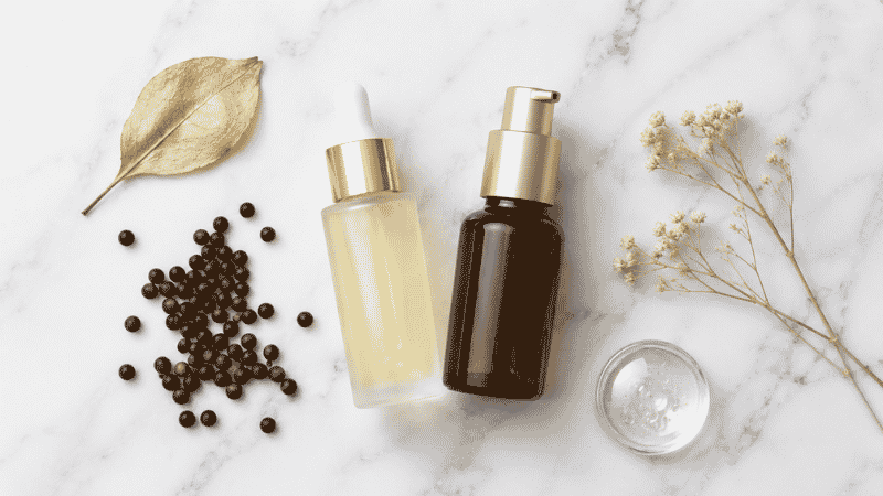 Bakuchiol serum in frosted glass beside amber retinol serum on white marble — bakuchiol vs retinol comparison for mature anti-aging skincare
