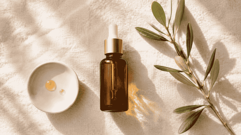 Luxury squalane face oil in amber dropper bottle on warm ivory linen with olive branch — squalane moisturizer guide for mature aging skin