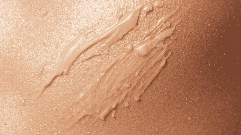 A high-definition macro shot of Armani Luminous Silk Foundation being blended into radiant skin, demonstrating its seamless, poreless finish and natural glow in bright daylight.