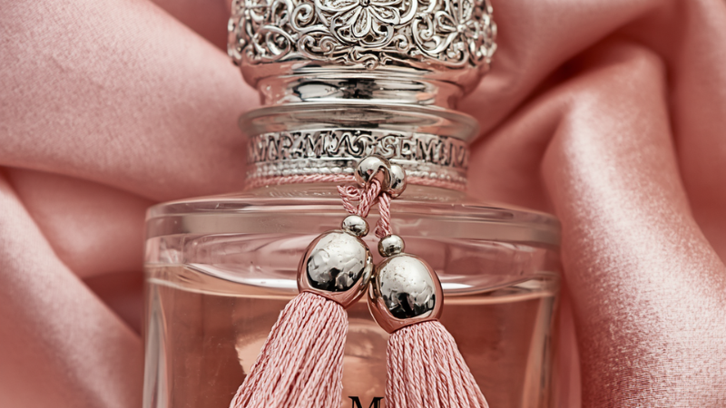 Macro shot of the intricate silver cap and signature pink silk tassels of the Delina perfume bottle, showcasing the premium craftsmanship and luxury texture of the Parfums de Marly packaging