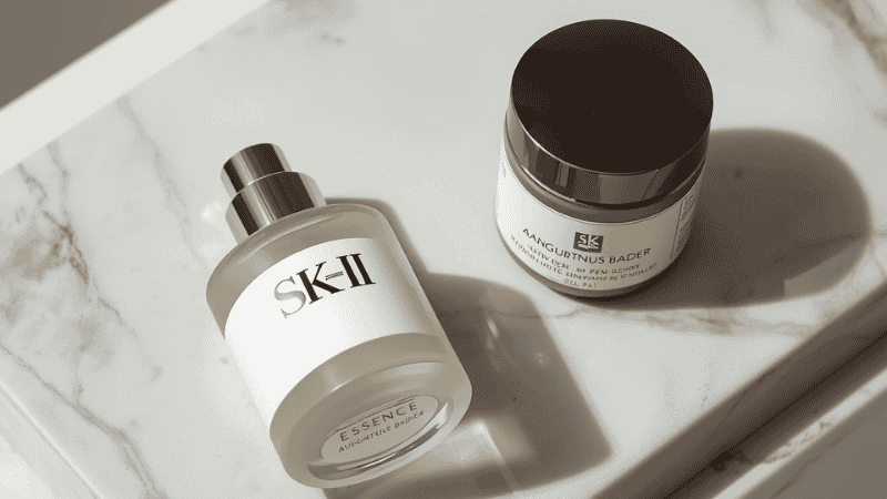A serene, high-end beauty vanity featuring luxury skincare bottles like SK-II Essence and Augustinus Bader cream resting on a white Calacatta marble slab in soft morning light.