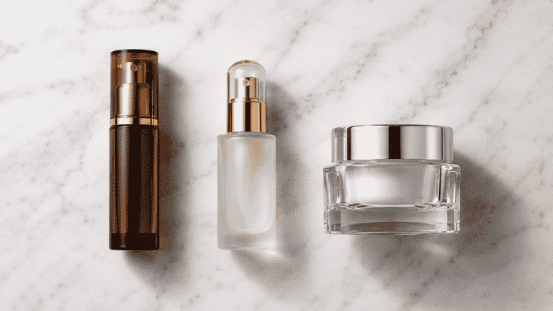 Three luxury skincare investment products — vitamin C serum, retinol and ceramide moisturiser on white marble — where to invest in luxury skincare routine for women over 40