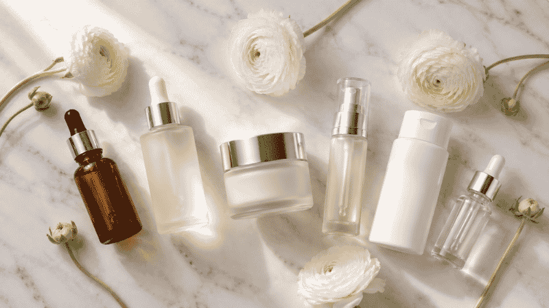 Complete luxury anti-aging skincare collection on white marble with ranunculus flowers — skincare for women over 40 complete guide including retinol, vitamin C, ceramides and SPF