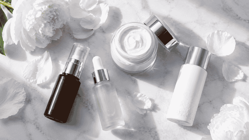Luxury vitamin C, retinol, ceramide and SPF skincare products on white marble with white peonies — skincare in your 30s complete anti-aging foundation guide